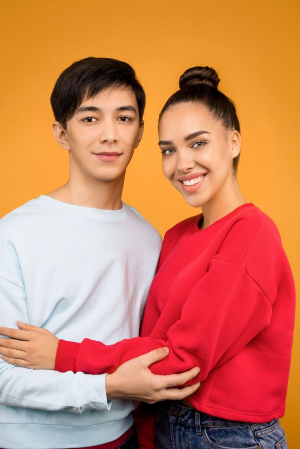 A smiling couple in front of an orange wall