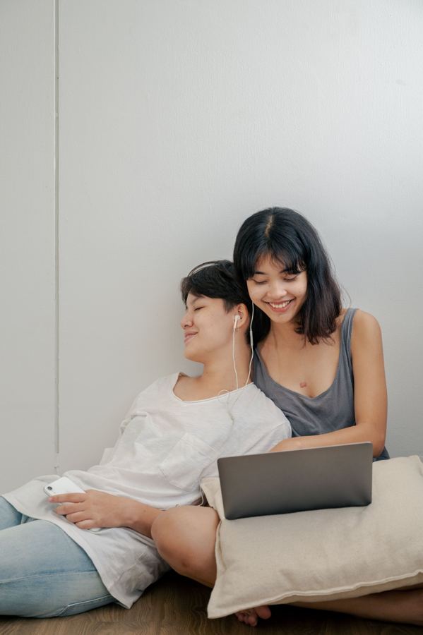 Two people relaxing against a wall with a laptop